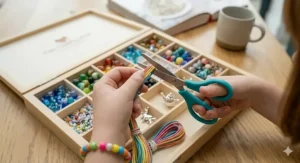 A close-up showing a child safely using the included teal-handled craft scissors to trim colourful elastic cord over the bead organiser.