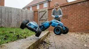 A photorealistic 4K image of a blue remote-control stunt robot performing a mid-air flip on a damp paved path in a British garden, controlled by the 8-year-old child from the hero image.