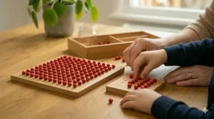 A close-up photo under soft, natural light, focusing on the adult and child’s hands placing red beads on a wooden hundred board Montessori maths grid to solve the multiplication problem '3x4'. They are completing skip counting patterns. A nearby board with numbers 1-100 is visible on the oak wood table.
