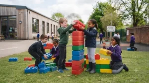 Young children working together to build a tall tower using giant outdoor building blocks.
